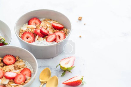 Photo for Chia pudding with homemade coconut granola, peanut butter and strawberries in gray bowl, marble background. Healthy plant based diet, detox, summer recipe. - Royalty Free Image