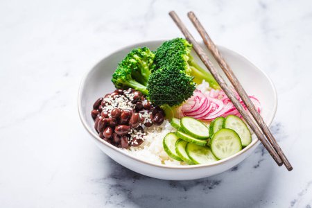 Vegan poke bowl with rice, broccoli, cucumber, beans and pickled red onion, white marble background.