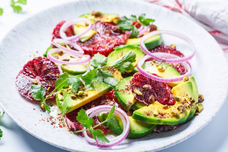 Blood oranges salad with avocado, pistachios and red onions, white background, close-up.