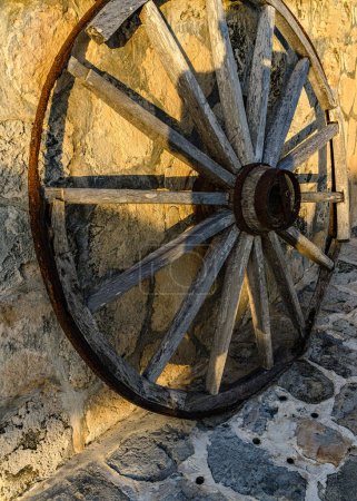 Téléchargez les photos : Roue de chariot en bois antique contre le mur de pierre dans la lumière dorée. - en image libre de droit