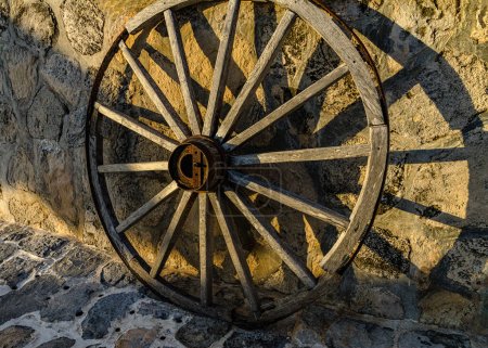 Téléchargez les photos : Roue de chariot en bois antique contre le mur de pierre dans la lumière dorée. - en image libre de droit