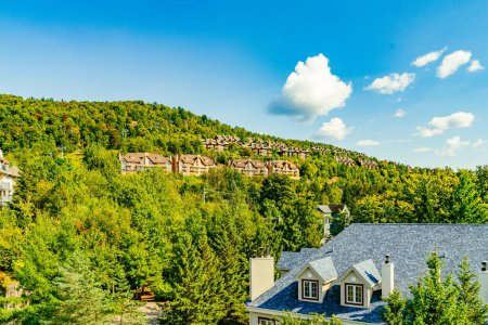 Lush greenery envelopes Mont Tremblants residential area, with charming houses perched on the hillside under a clear blue sky, capturing the essence of the beautiful national park. Quebec, Canada