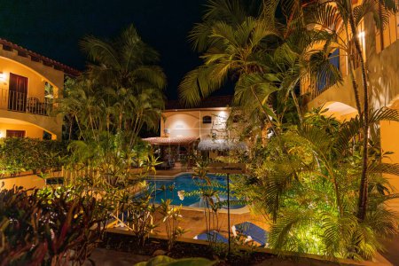 Ein einladender Hotelpool in Playa Hermosa liegt inmitten pulsierender tropischer Pflanzen, die von Umgebungslichtern beleuchtet werden, die eine ruhige Abendoase in der Provinz Guanacaste, Costa Rica, schaffen. Hohe Qualität