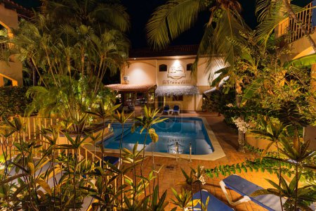 An inviting hotel pool area in Playa Hermosa is nestled among vibrant tropical plants, illuminated by ambient lights that create a serene evening oasis in Guanacaste Province, Costa Rica. High quality