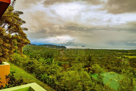 Eine unbefestigte Straße schlängelt sich durch die lebhaften grünen Hänge von Uvita in der Provinz Puntarenas, Costa Rica, unter einem nebligen Himmel und fängt die dynamische Interaktion zwischen menschlicher Siedlung und dem üppigen