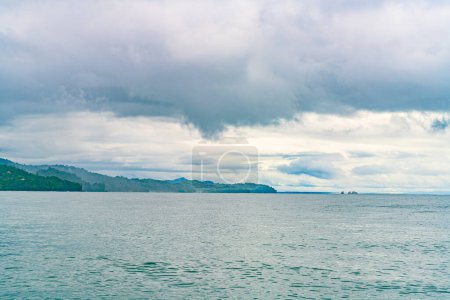 Tranquil ocean waters before a tropical coastline with clouds descending upon verdant hills. High quality photo. Uvita Puntarenas Province Costa Rica.