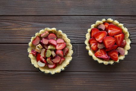 Delicious strawberry and rhubarb tarts on brown wooden background, top view. 