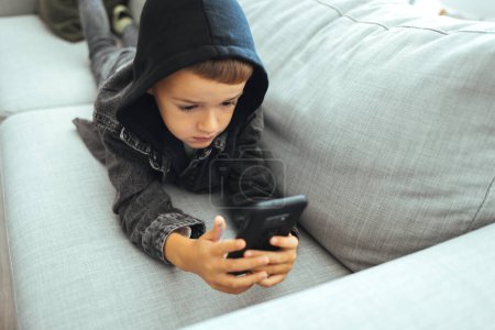 Photo for Close up of cute little 7s Caucasian boy child look at cellphone screen play online game on gadget. Small preschooler kid have fun using smartphone device with wireless internet connection. - Royalty Free Image
