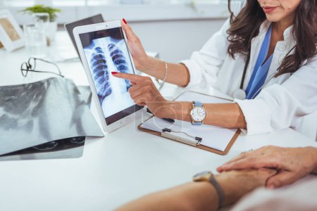 Photo for Doctor shows results to old patient x-ray of the lungs, smoking cigarettes problem. Doctor explaining lungs x-ray on Tablet PC screen to young patient. Doctor showing female patient x-ray shot in clinic office. Coronavirus chest X-ray. - Royalty Free Image