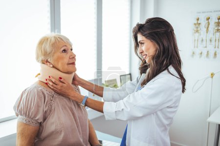 Photo for Portrait of a female doctor helping a senior woman at office with her neck injury a healthcare and medicine concepts. Doctor putting neck orthopaedic collar on adult injured woman - Royalty Free Image