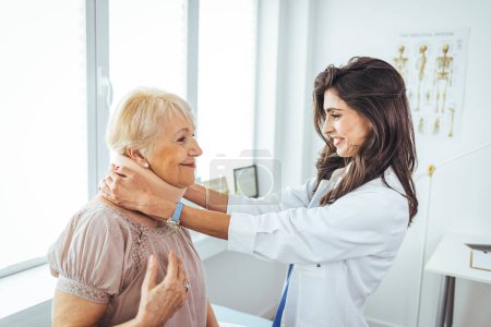 Photo for Female doctor putting neck orthopaedic collar on adult injured woman. Woman in pain at the doctor for a neck injury. Doctor giving a prescription to a senior patient with cervical collar - Royalty Free Image