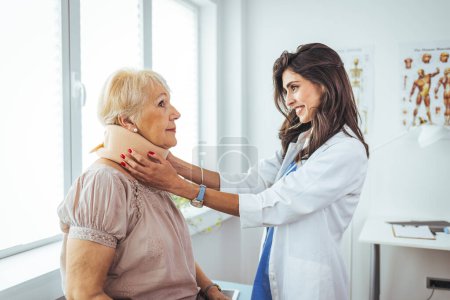 Photo for Female doctor putting neck orthopaedic collar on adult injured woman. Doctor talking to a senior patient with cervical collar at the hospital. Doctor applying cervical collar on neck of woman in clinic - Royalty Free Image