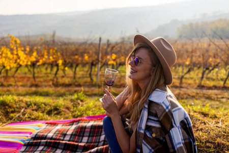 Photo for Winery at autumn. Portrait of pretty young woman holding glass of wine and enjoying in vineyard. Beautiful woman enjoying in wine. Walking through my vineyard. - Royalty Free Image
