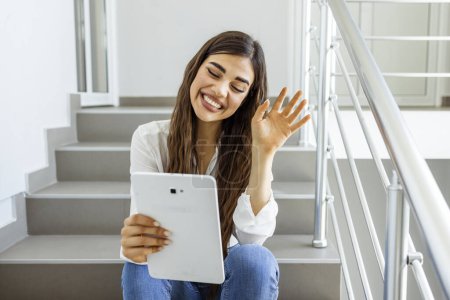 Photo for Female student sitting on stairs with a tablet pc. Young female college student using tablet on a staircase. College girl using tablet. Staying updated with current affairs - Royalty Free Image