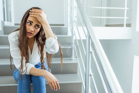 Photo for Depressed sad woman sitting on the stairs of a business building, businesswoman in business clothes tired. Business woman stressed from work while sitting indoors on the stairs - Royalty Free Image