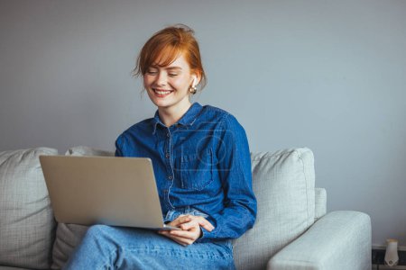 Photo for Young woman with laptop and glasses sitting on sofa at home - Royalty Free Image