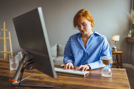 Photo for Young female employee busy working on computer typing writing business letter to client - Royalty Free Image