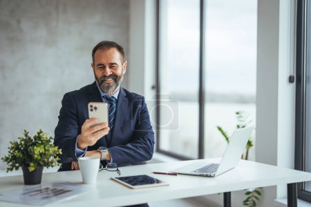 Photo for Caucasian businessman using smartphone while working at desk in office - Royalty Free Image