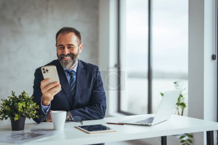Photo for Caucasian businessman using smartphone while working at desk in office - Royalty Free Image
