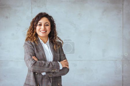 Téléchargez les photos : Portrait de jeune femme souriante regardant la caméra avec les bras croisés. Bonne fille debout dans un bureau créatif. Femme d'affaires prospère debout dans le bureau avec espace de copie. - en image libre de droit