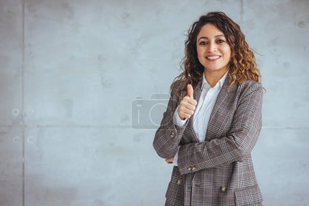 Photo for Portrait of middle aged businesswoman in modern office looking at camera. Confident business woman with arms crossed standing while leaning against glass wall. Proud brunette woman smiling in formalwear with copy space. - Royalty Free Image