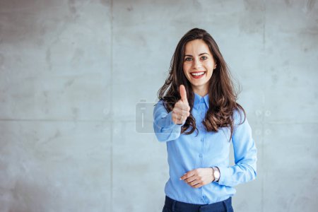 Photo for Happy businesswoman showing thumb up over gray background. Wearing in blue shirt. Looking at camera. Like. Joyful Office Girl Gesturing Thumbs Up Standing On Gray Background. Studio Shot - Royalty Free Image