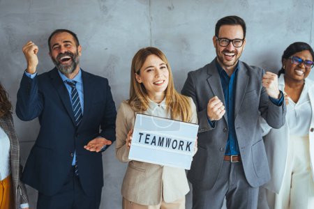 Photo for Portrait of multi ethnic successful business team looking at camera in the office and team leader holding sign ''teamwork'' in hands. Positive team motivation. Diverse creative team looking happy - Royalty Free Image