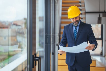 Téléchargez les photos : Portrait d'un ingénieur tenant un plan sur un chantier de construction alors qu'il portait un casque. Travailleur de la construction avec casque sur le chantier de construction examinant les plans de bureau. À l'intérieur - en image libre de droit
