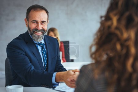 Photo for Businessman shaking a womans hand in the office. Happy businessmen on a job interview in the office. Focus is on mature businessman shaking hands with a candidate. - Royalty Free Image
