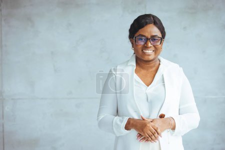 Téléchargez les photos : Portrait d'une belle femme d'affaires afro-américaine souriante et confiante, les bras croisés dans le bureau et regardant la caméra. Femme d'affaires afro-américaine souriante portant des lunettes élégantes regardant la caméra - en image libre de droit