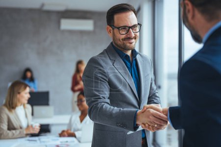 Photo for Portrait of cheerful young manager handshake with new employee. Business partnership meeting in office. Close up of handshake in the office. Mature businessman shake hands with a younger colleague - Royalty Free Image