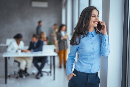 Photo for Smiling businesswoman using phone in office. Small business entrepreneur looking at her mobile phone and smiling. Beautiful smiling businesswoman using smarphone indoors, copy space. - Royalty Free Image