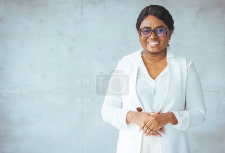 Photo for Portrait of young cheerful african american woman wearing White suit smiling and looking at camera. Shot of a confident young businesswoman working in a modern office. - Royalty Free Image