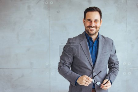 Photo for Young handsome business man, isolated on gray background. Portrait of handsome confident smiling businessman standing with arms crossed in the office and looking at camera. - Royalty Free Image