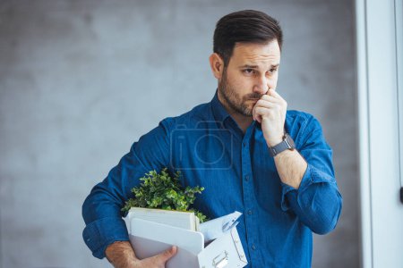 Photo for He just got his marching orders. Shot of a stressed businessman holding his box of possessions after getting fired from his job. Young handsome businessman in light modern office with carton box. - Royalty Free Image