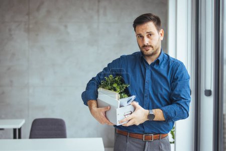 Photo for Unemployed guy in formal wear holding personal belongings, feeling depressed after losing his job. Upset Eastern man with cardboard box of things leaving office after being fired - Royalty Free Image