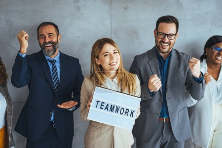 Photo for Portrait of multi ethnic successful business team looking at camera in the office and team leader holding sign ''teamwork'' in hands. Multi-ethnic group of business persons standing side by side - Royalty Free Image