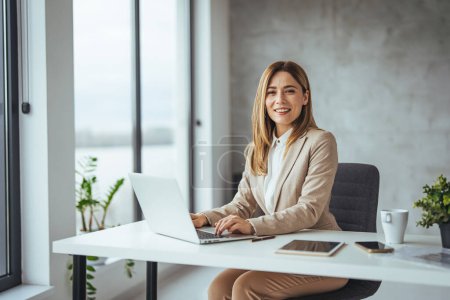 Photo for Successful business woman working at the office. Portrait of smiling pretty young business woman in glasses sitting on workplace. Portrait of a cheerful businesswoman sitting at the table in office and looking at camera - Royalty Free Image