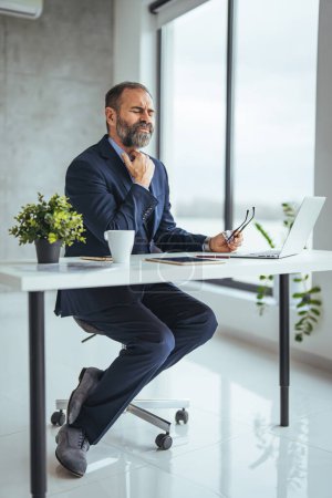 Photo for Mature man having stressful time working on laptop.  Man working with laptop and paperwork with stress. Exhausted businessman using laptop at work and sitting by the desk while - Royalty Free Image