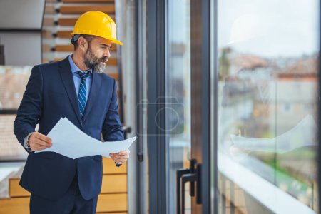 Photo for Portrait of an architect builder studying layout plan of the rooms, serious civil engineer working with documents on construction site, building and home renovation, professional foreman at work - Royalty Free Image