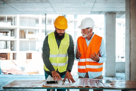 Téléchargez les photos : Ingénieurs caucasiens masculins ou architectes parlant pendant le travail avec le plan directeur sur le chantier de construction - en image libre de droit