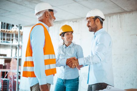 Foto de Arquitecta o ingeniera mirando a colegas masculinos estrechando las manos en el sitio de construcción - Imagen libre de derechos
