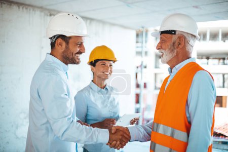Foto de Arquitecta o ingeniera mirando a colegas masculinos estrechando las manos en el sitio de construcción - Imagen libre de derechos