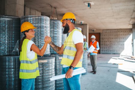 Photo for Young caucasian architects or engineers handshaking at construction site with blurred colleagues on background - Royalty Free Image