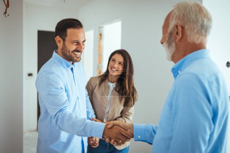 Photo for Lovely married couple, looking to buy a new apartment with a help of a real estate agent. Real Estate Agent showing a house under construction to a couple and greeting them with a handshake - Royalty Free Image