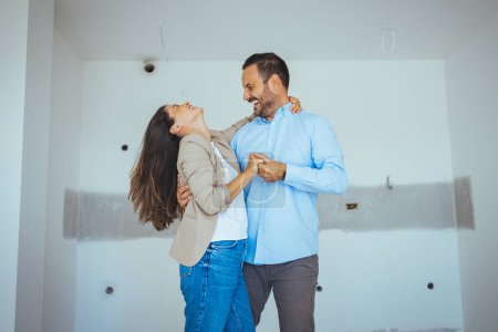 Téléchargez les photos : Couple dansant heureux avec appartement choix. Déménagement, immobilier, concept de loyer. Heureux et excité jeune couple regarder autour de lui dans l'émerveillement à leur nouvellement acheté - en image libre de droit