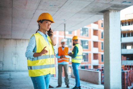 Photo for Construction woman closing deal on the phone. Portrait of civil engineer woman doing business, talking on smartphone and holding tablet computer in hand, standing against high buildings and tower cranes at a construction site. - Royalty Free Image