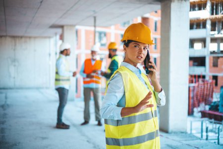 Photo for Caucasian businesswoman talk on phone while work. Gorgeous caucasian female architect in yellow west and with protective helmet on standing at construction site and using smart phone. - Royalty Free Image
