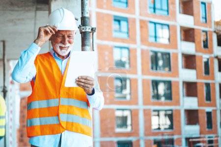 Photo for Engineer at construction site, using digital tablet. Mature man working on digital tablet at construction site. Portrait of male engineer with hardhat using digital tablet while working at construction site - Royalty Free Image