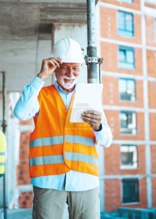 Photo for Construction Worker Planning Contractor Developer Concept. Serious and focused architect or engineer working on construction site using digital tablet while wearing safety vest and helmet - Royalty Free Image